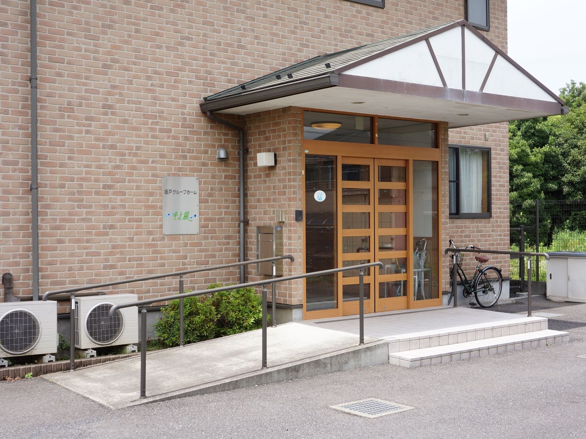 玄関ポーチには屋根がある。階段と別にスロープが用意され、手すりが設置されている。壁に看板が取り付けられている。