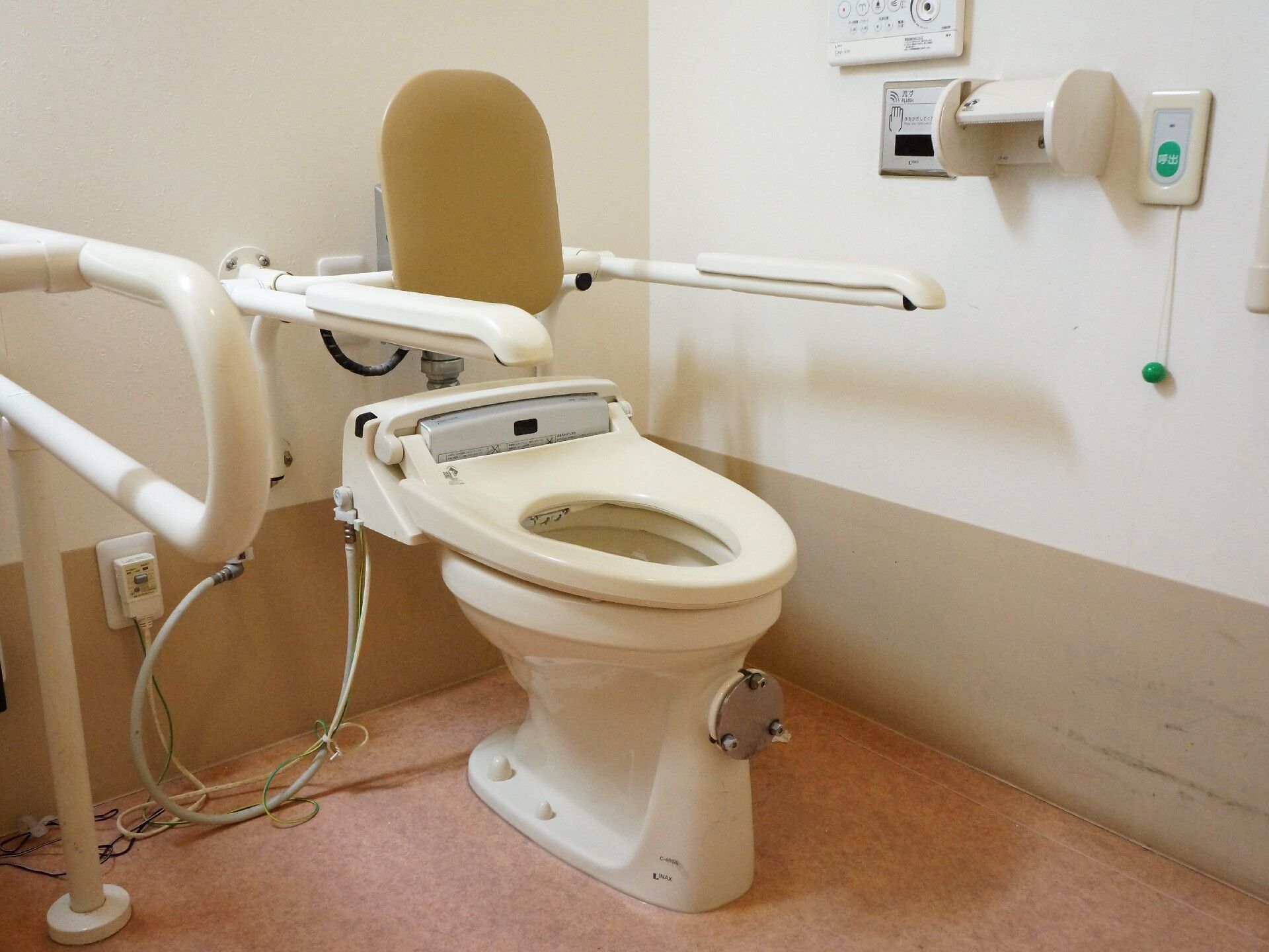 車いす対応の広いトイレ。トイレには手すりと背もたれが付き、車いすの方用に洗面所下のスペースが開けられている。