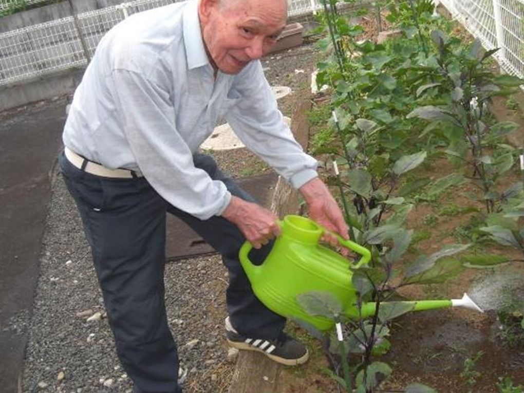 じょうろを持ち、うれしそうな表情でナスなどの夏野菜に水やりをする男性入居者。