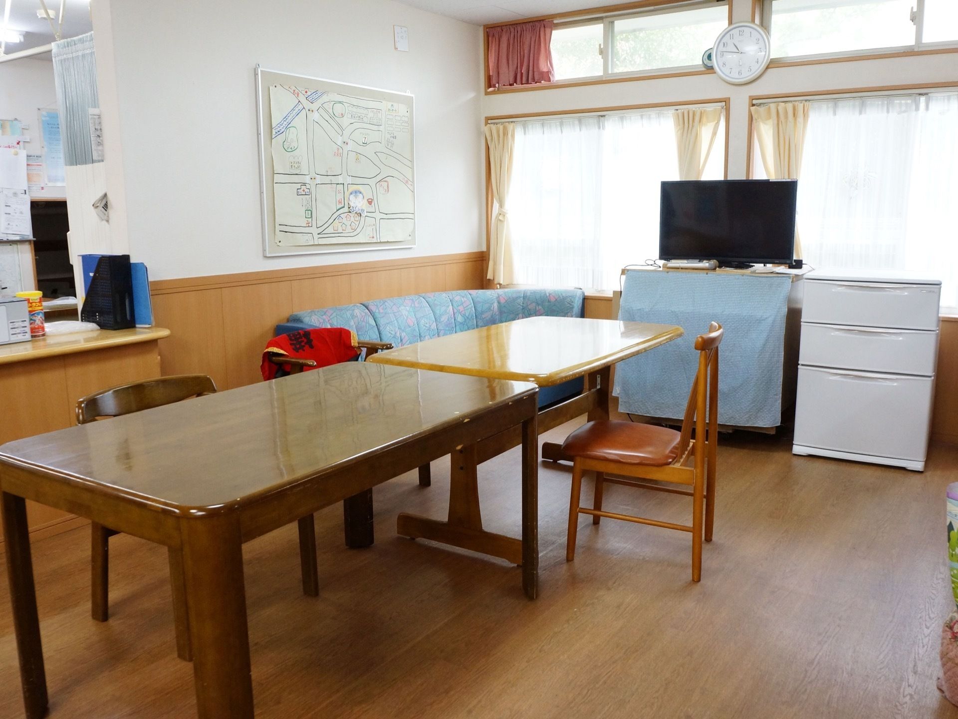 共有スペースの壁に手作りの近隣マップが貼られている。テーブルセットとソファ、液晶テレビが置かれている。