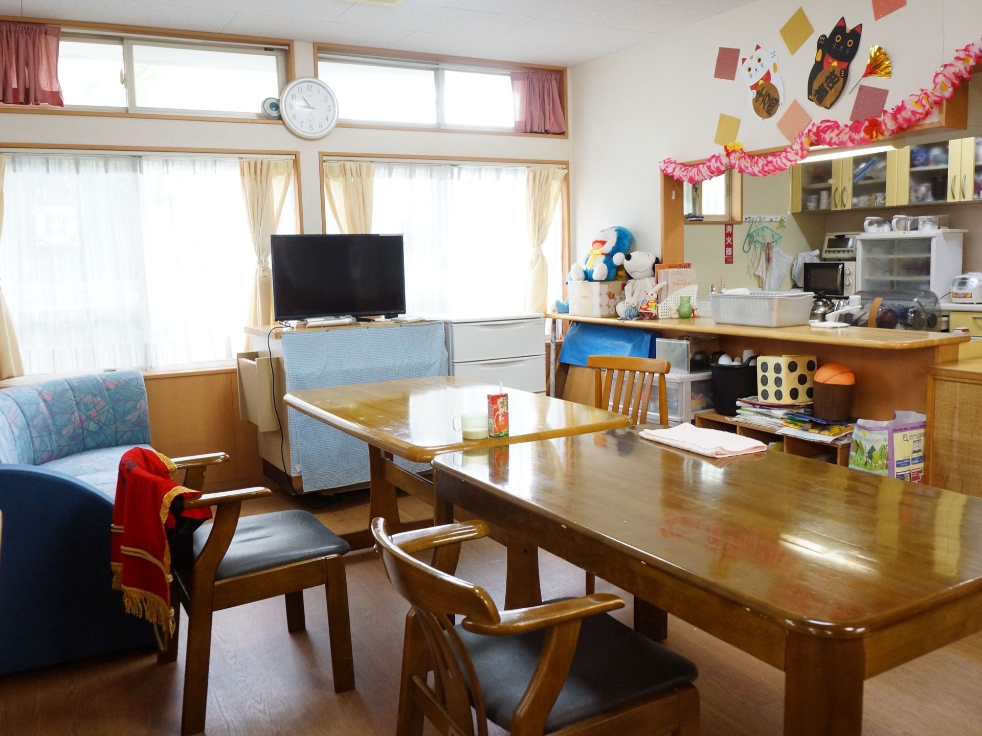 キッチンが併設された共有スペースになっている。壁には縁起物の飾り付けがされ、キャラクターのぬいぐるみが置かれている。