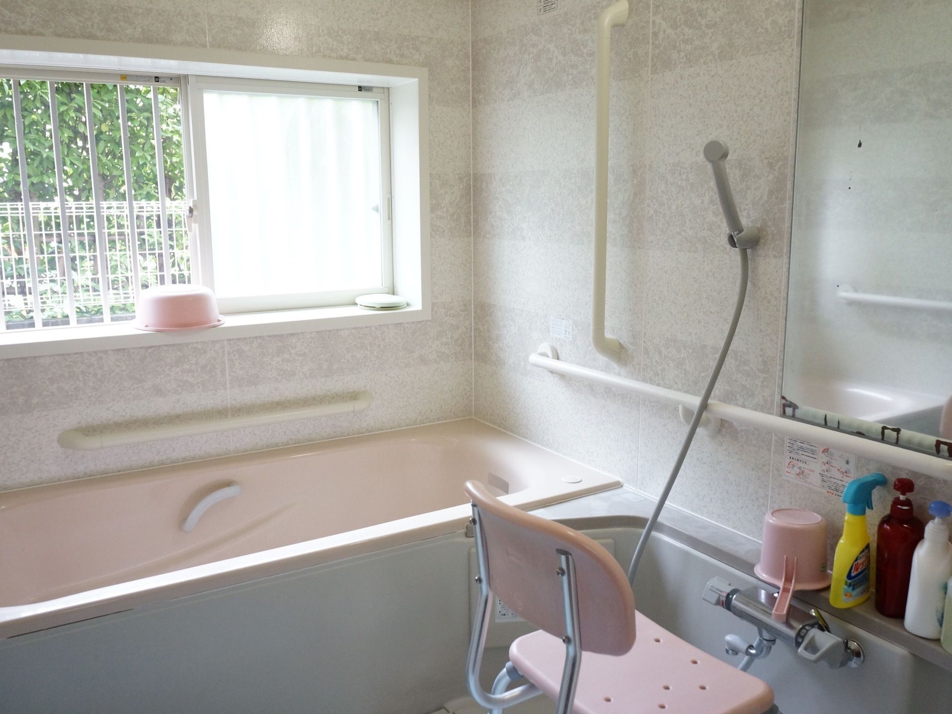 個浴用浴室の壁には手すりが多数設置されている。介護用椅子が１脚あり、手桶やシャンプー類が用意されている。