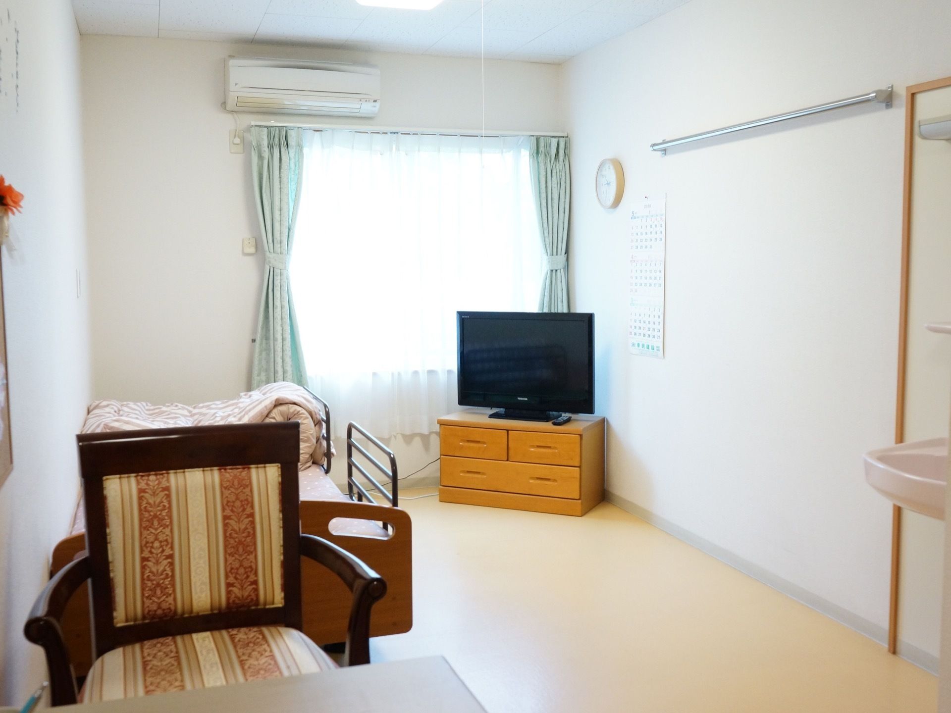 居室には介護用ベッドが用意されている。テレビ台の上に液晶テレビが置かれ、窓の上にはエアコンが完備されている。