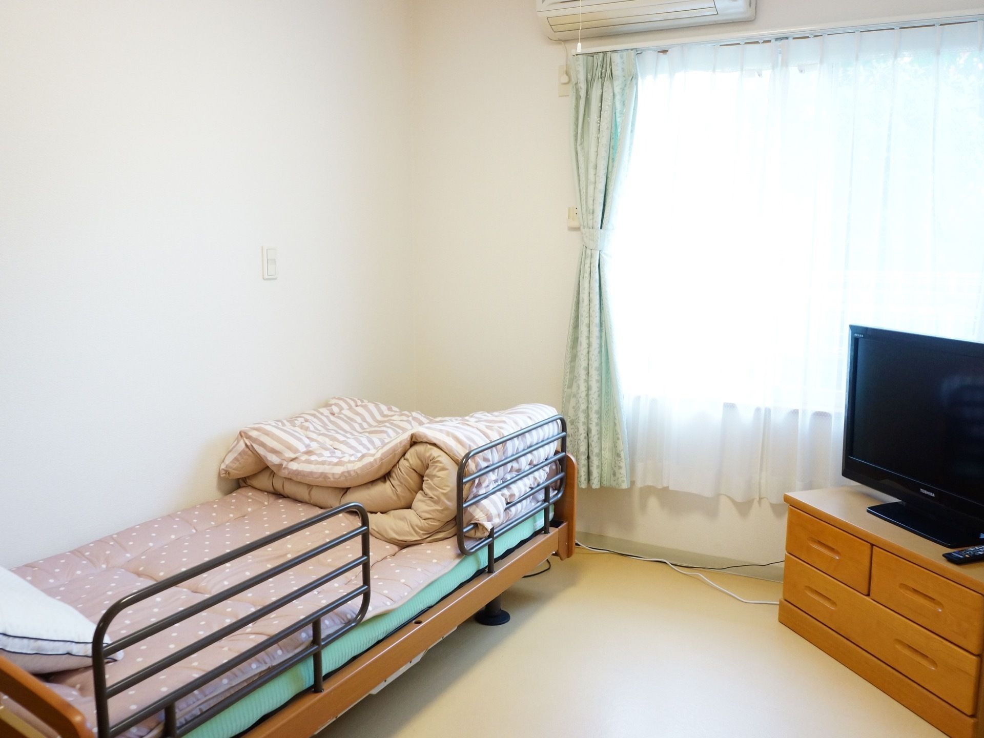 居室内のベッドは、落下防止の手すりの付いた介護用のものを用意している。ベッドに横になったままテレビが見られる。