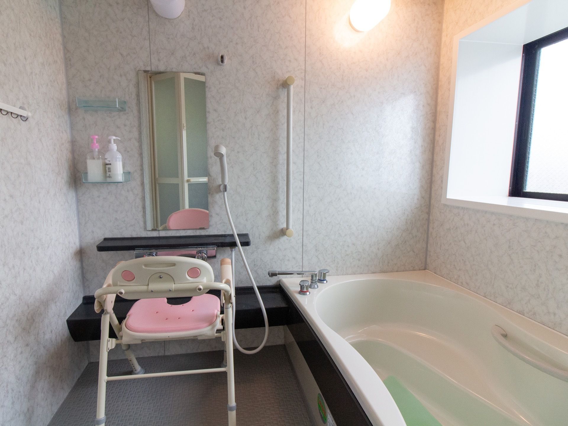 一人で入浴できるタイプの浴室である。淡いグレーの模様の入った壁で、洗い場にシャワーチェアが置かれている。
