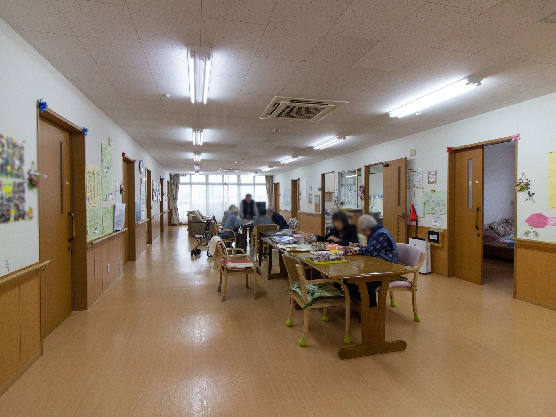 両サイドの壁に居室のドアが並んでおり、中央部分にテーブルがいくつも並んでいる。奥の窓際にテレビが置かれている。