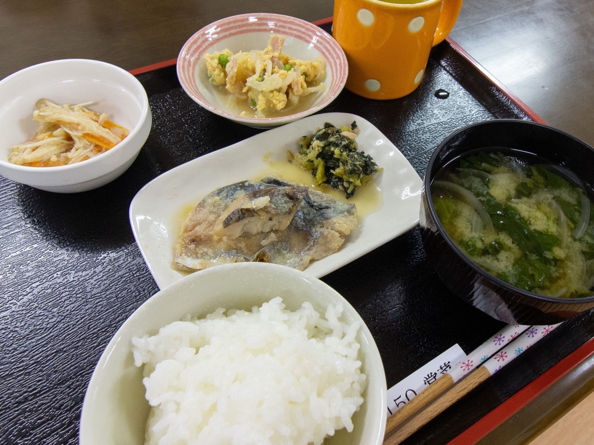 黒色のトレーにご飯、味噌汁のほか、おかずが４種類盛りつけられている。多くの食材が使用された食事である。