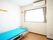 青いマットレスの敷かれたベッドが置いてある白い壁の部屋