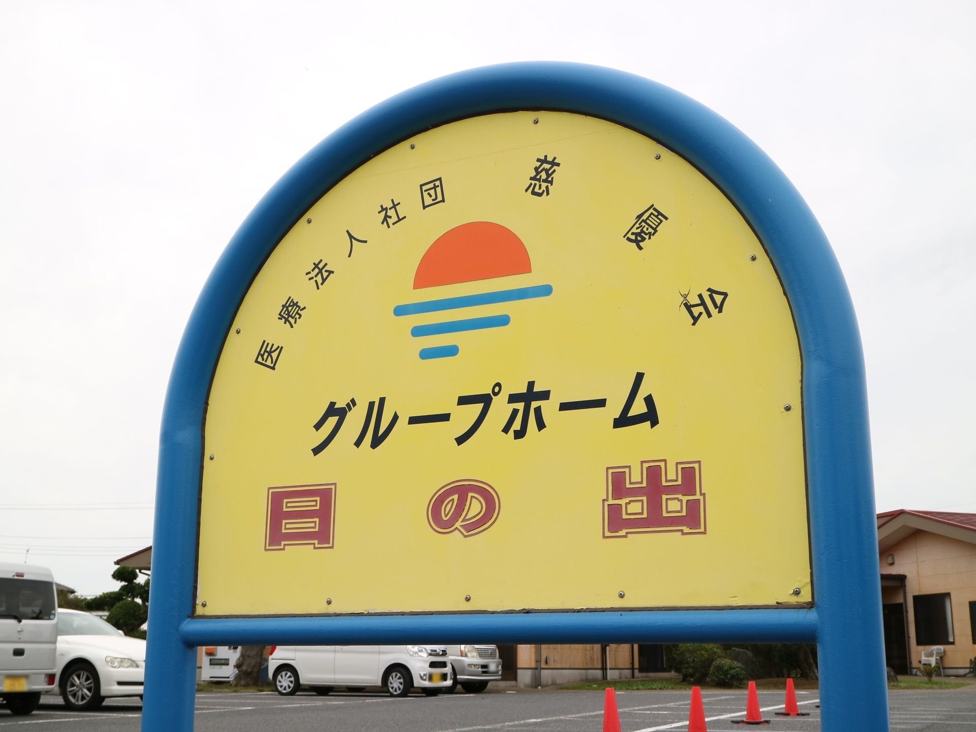 バスの停留所を思わせるような鉄製の看板である。施設の名前が日の出の絵とともに、高い場所に掲げられている。