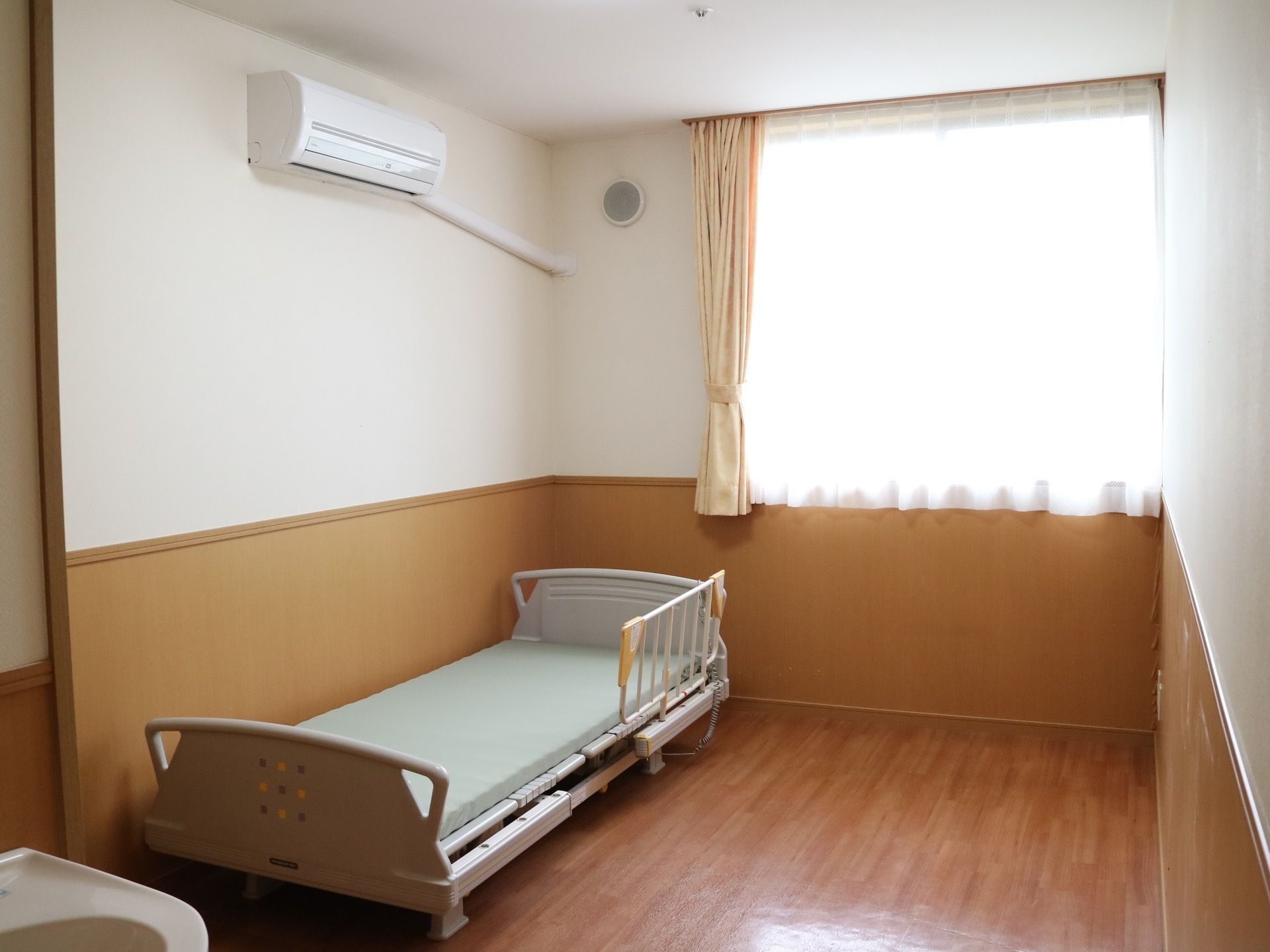 木目調の床色に施された、フローリング部屋である。壁には腰板が設置されている。エアコンやベッドがある。