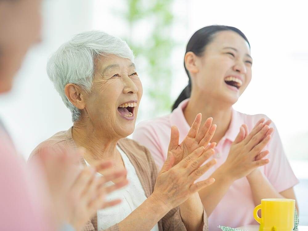 手を叩いて笑う高齢女性と女性スタッフ