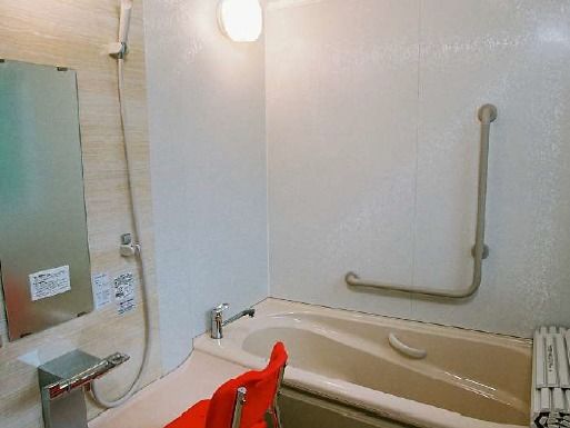 浴槽内と外に手すりが付き、安全に配慮された浴室。浴室左手には赤いシャワーチェアとシャワー、鏡が設置されている。