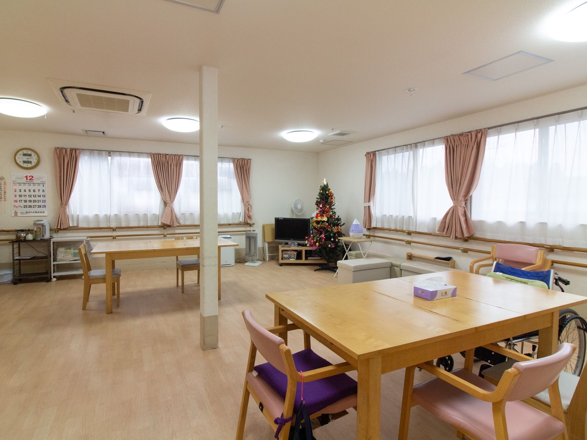 横に広い窓が並ぶ広々とした食堂に、テーブルが余裕を持って置かれている。部屋の角にテレビやクリスマスツリーがある。