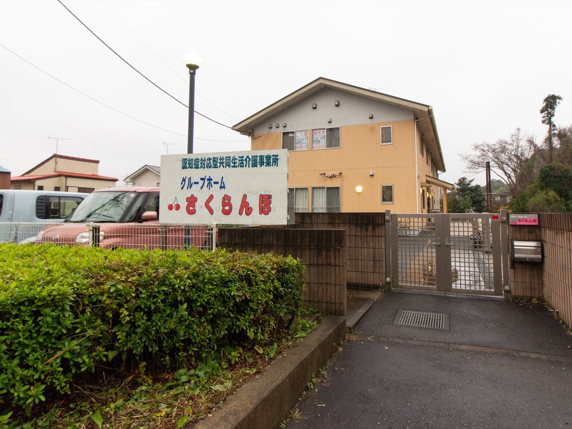 ２階建ての、明るいオレンジ色の壁の建物である。門扉の外側に駐車スペースがあり、施設名の書かれた看板が立っている。
