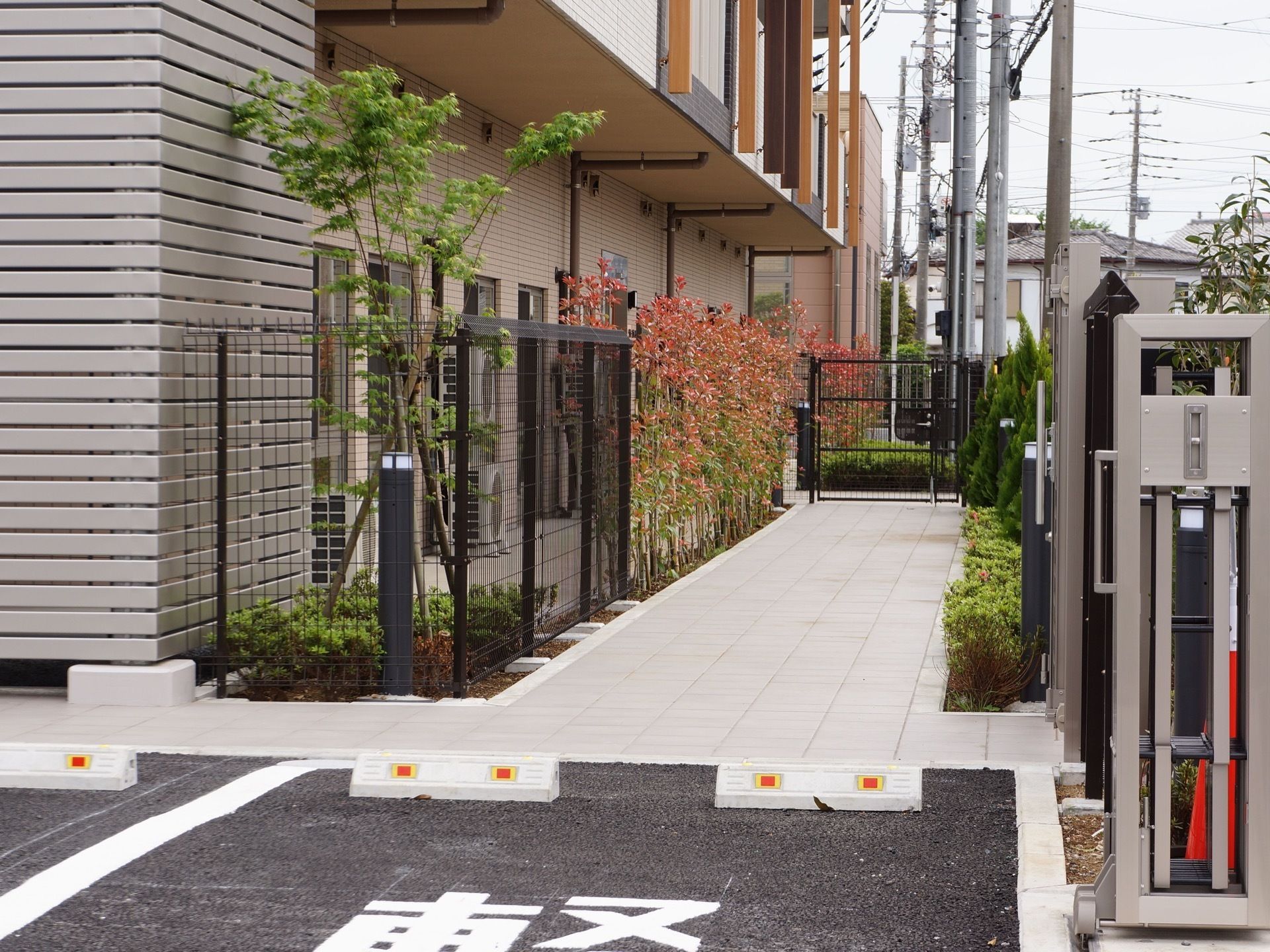施設の駐車場スペースから玄関までが写っている。施設の周りには木が植えてある。施設の周りは住宅地である。