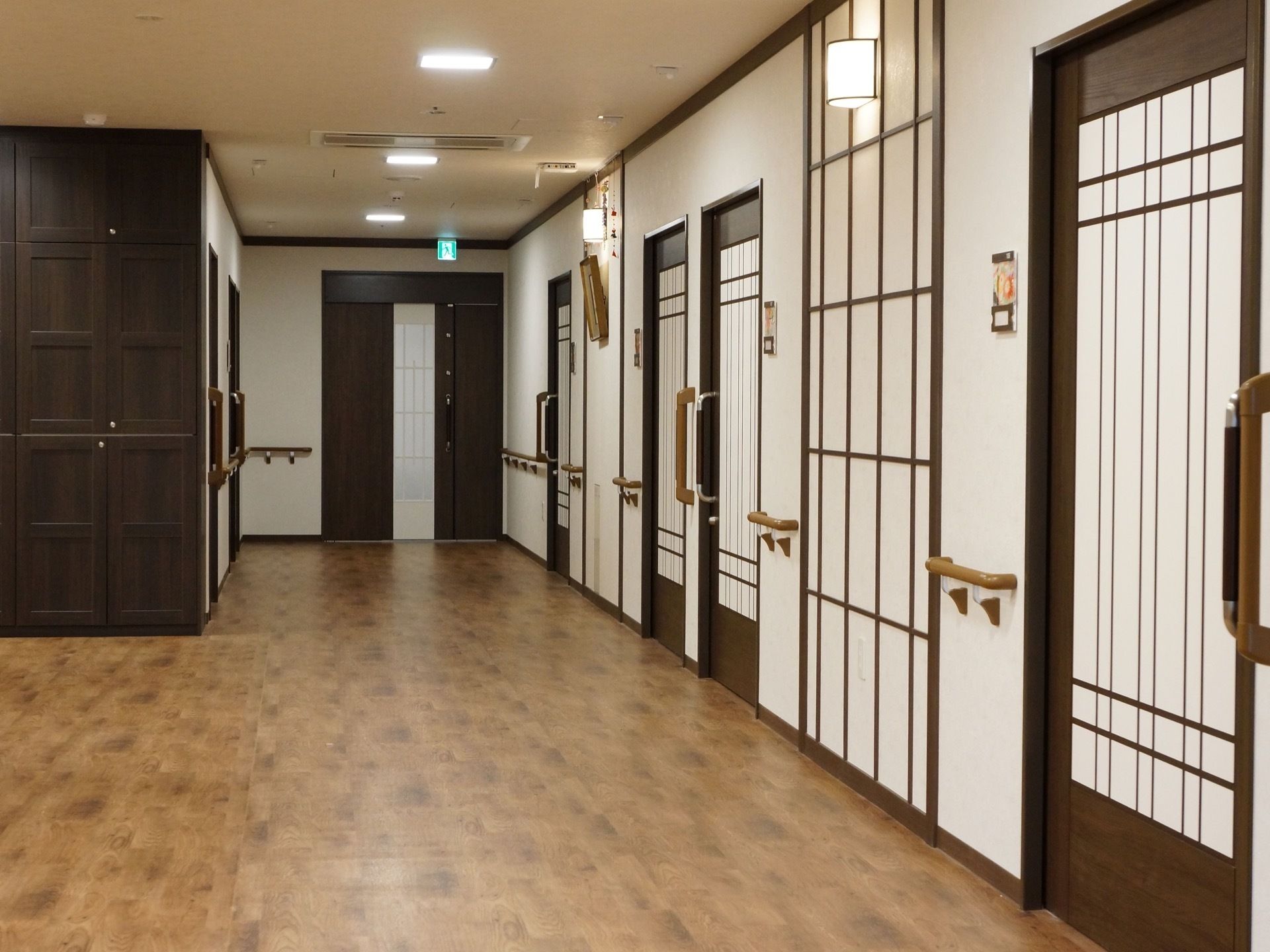 広々としたフローリングの廊下。壁には手すりが設置され、ダークブランを基調としたドアは開けやすいように引き戸になっている。