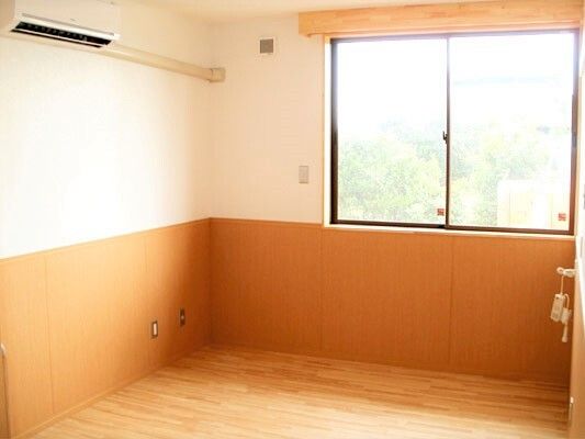 大きな窓が付いた明るい居室。右の壁には緊急通報装置が設置され、左上の壁にはエアコンが付いている。