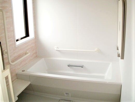 手すりが付いた明るい浴室は、白を基調としていて壁の一面に白とピンクの模様がある。大きな窓も付いている。