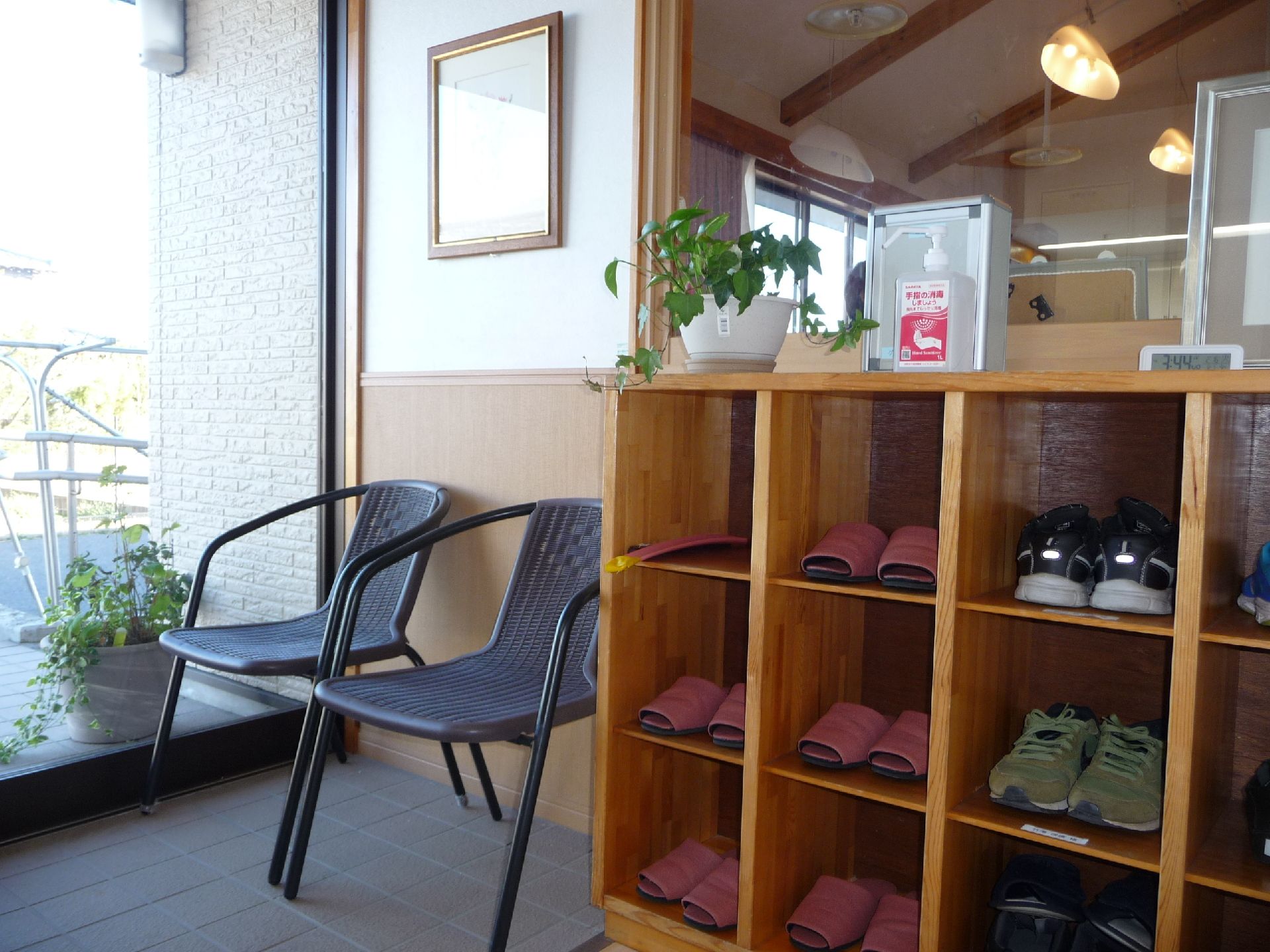 ベージュの外壁に緑の三角屋根が付いた平屋建ての建物。玄関には手すり付きのスロープがあり、車も敷地内に止まっている。