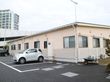 オレンジ色の外壁の施設が右奥に建っている。施設の周囲は駐車スペースが広がっており、軽自動車が１台停まっている。