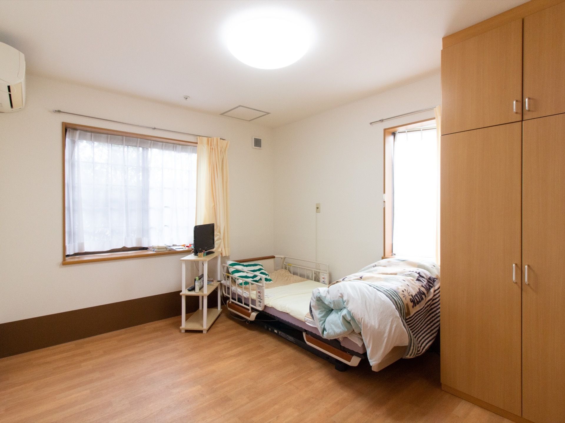正面と横側に窓があり、壁際に介護用ベッドを置いている。大きな両開きのクローゼットを設置し、エアコンを完備している。