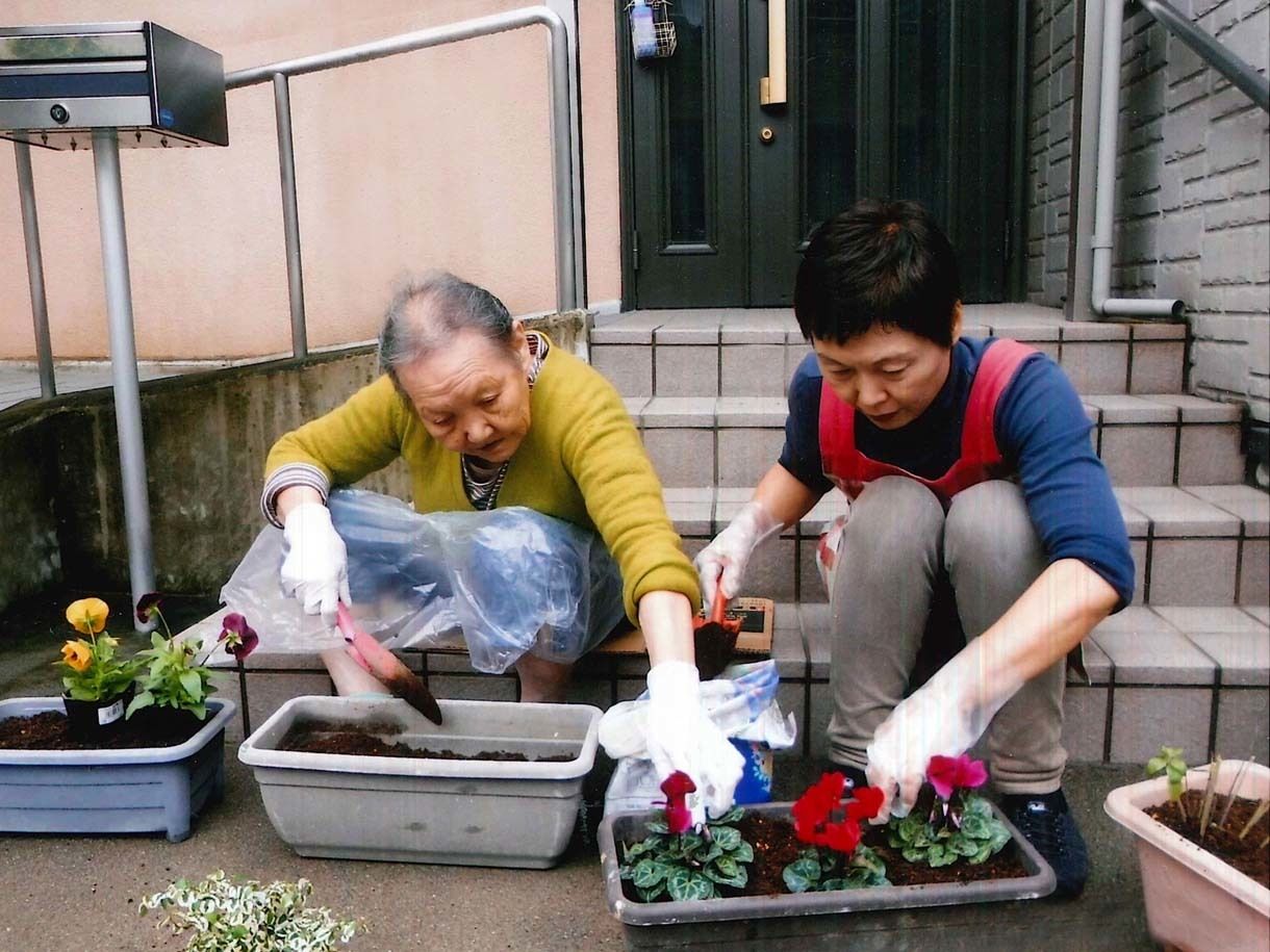 施設の外に出て花壇を作っている様子。プランターに花の苗を植えている高齢者とスタッフ