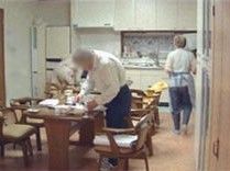 回転式のいすが設置されたダイニングテーブルで食事の手伝いをする入居者。奥にはキッチンがある。