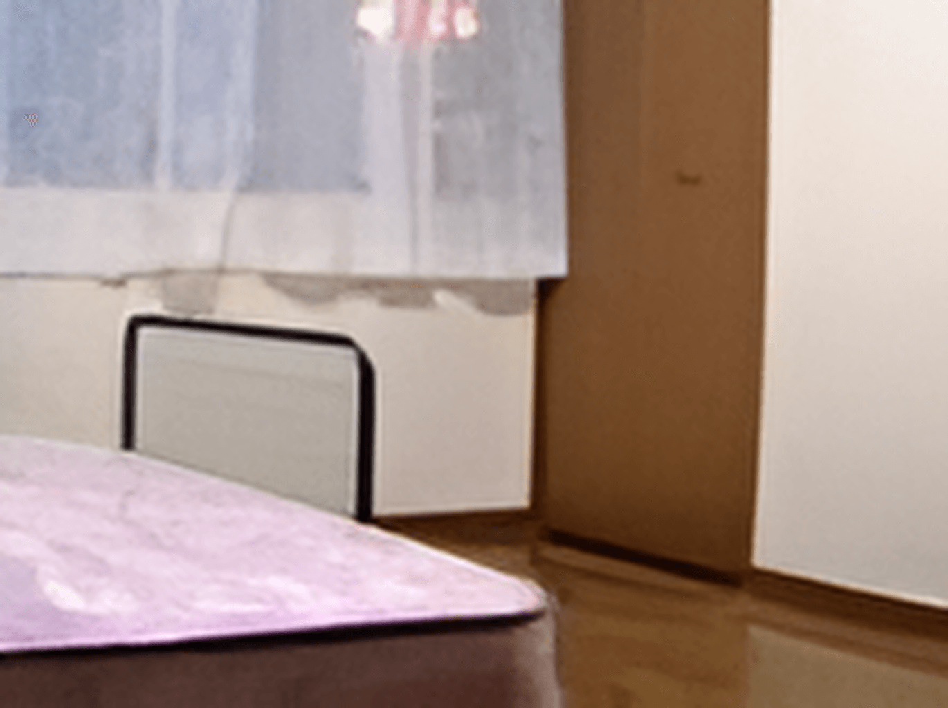 ベッドが設置された居室の窓にはレースカーテンが付けられている。フローリングの段差のない部屋。