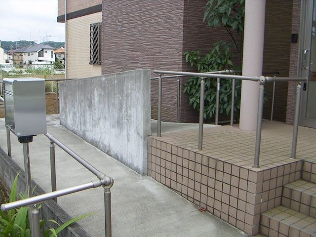 手すりが設置されたスロープが左側に、右側には階段が設置され、シルバーの郵便ポストもある。