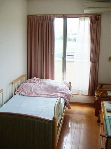大きな窓が付いたフローリングの部屋にはエアコンや介護ベッドが置かれ、フロアはフローリング。