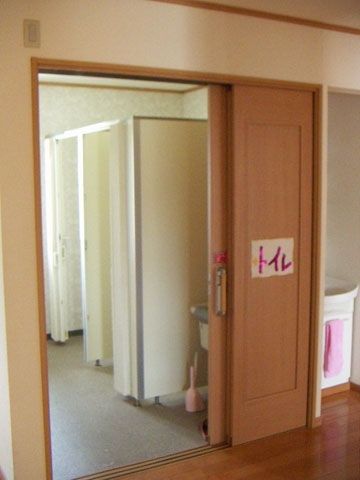 カーテンで開け閉めするタイプが二つ設置されたトイレは明るい雰囲気。ドアには手書きで「トイレ」と書かれた紙が貼られている。