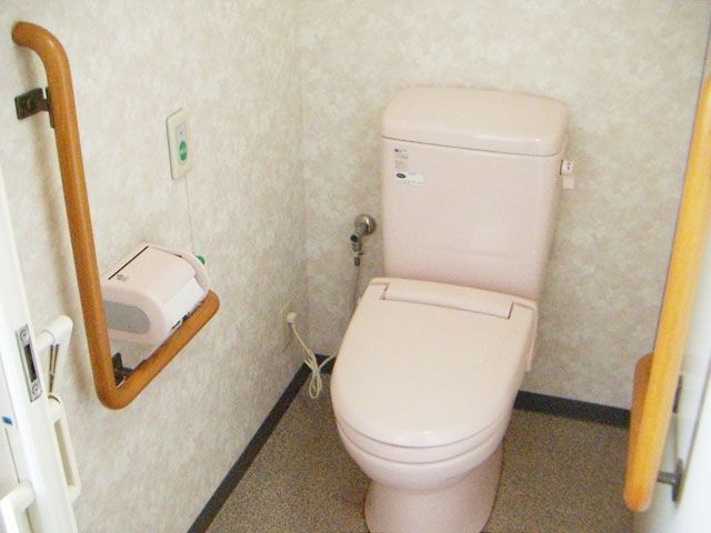 グリーンの呼び出しボタンが設置され、両サイドに手すりが設置されたトイレ。便座は薄いピンク。