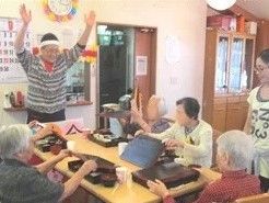 万歳をして話しかけているスタッフとそれにこたえる高齢者の様子。施設内のレクリエーション