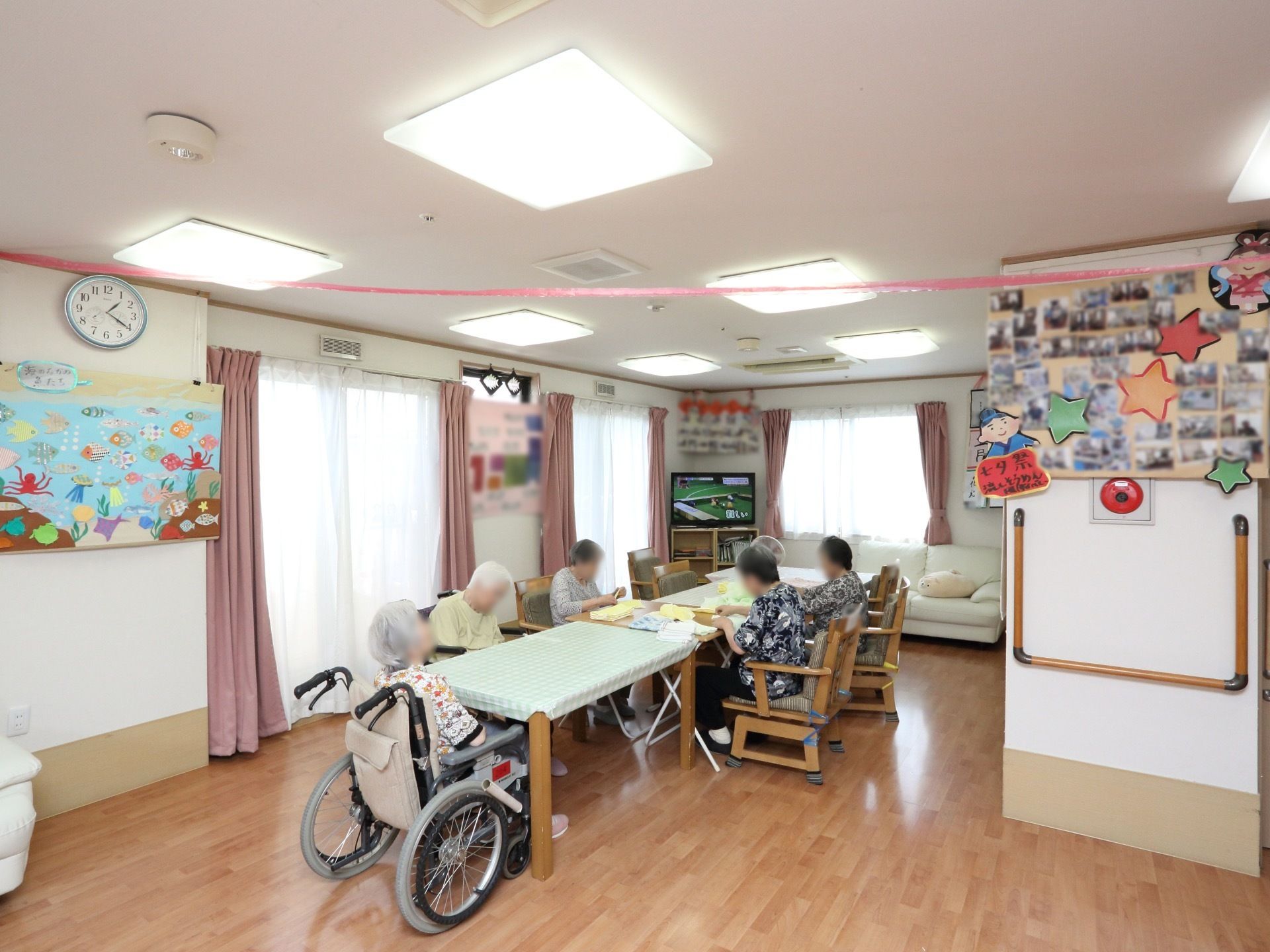 壁にたくさんの写真や手作りの作品が飾られている談話室。大きなテーブルを囲んで、入居者様たちが工作をされている。