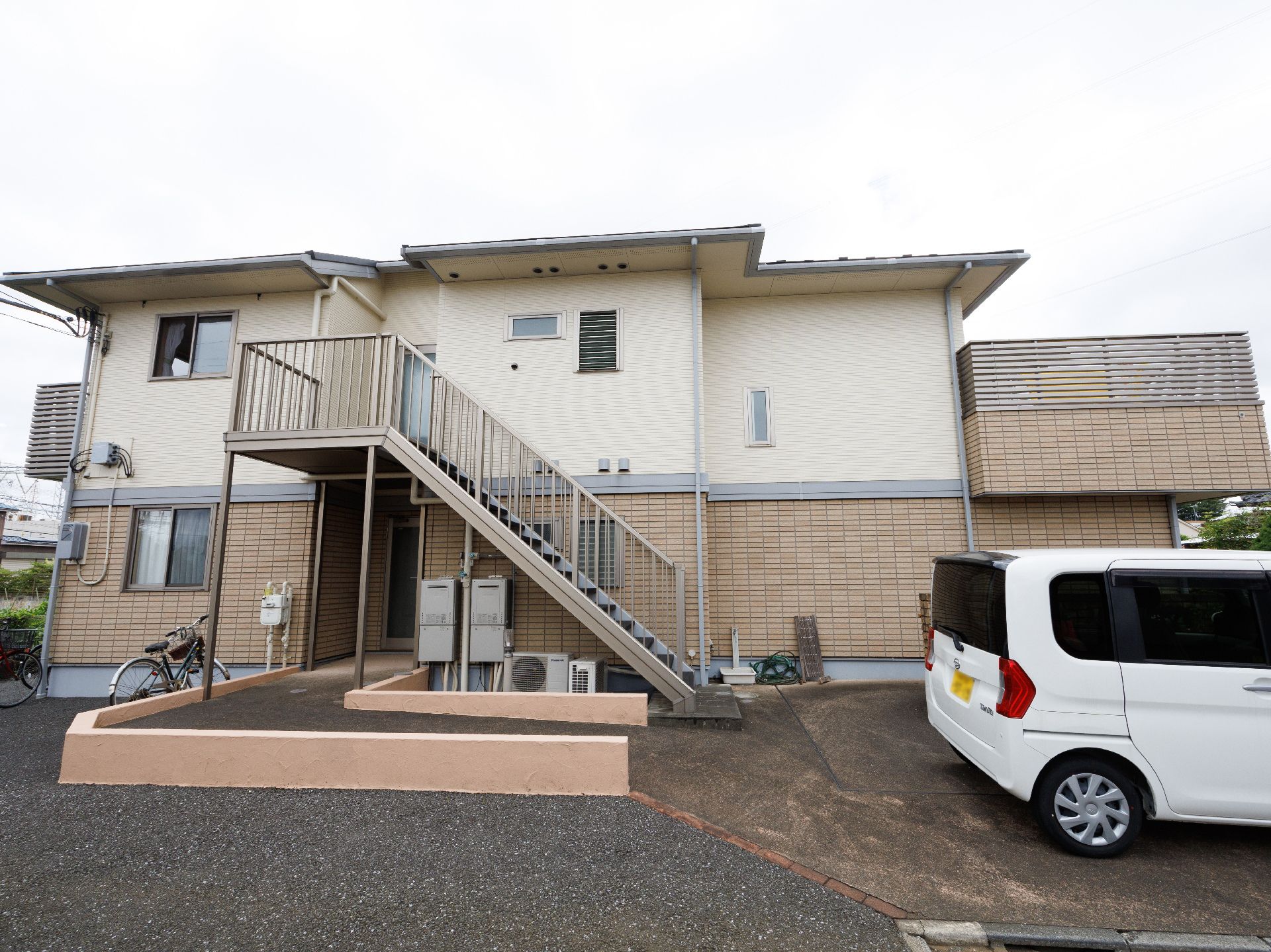 オレンジのカーディガンを着た車いすの高齢女性に白衣を着た女性スタッフが付き添っている。
