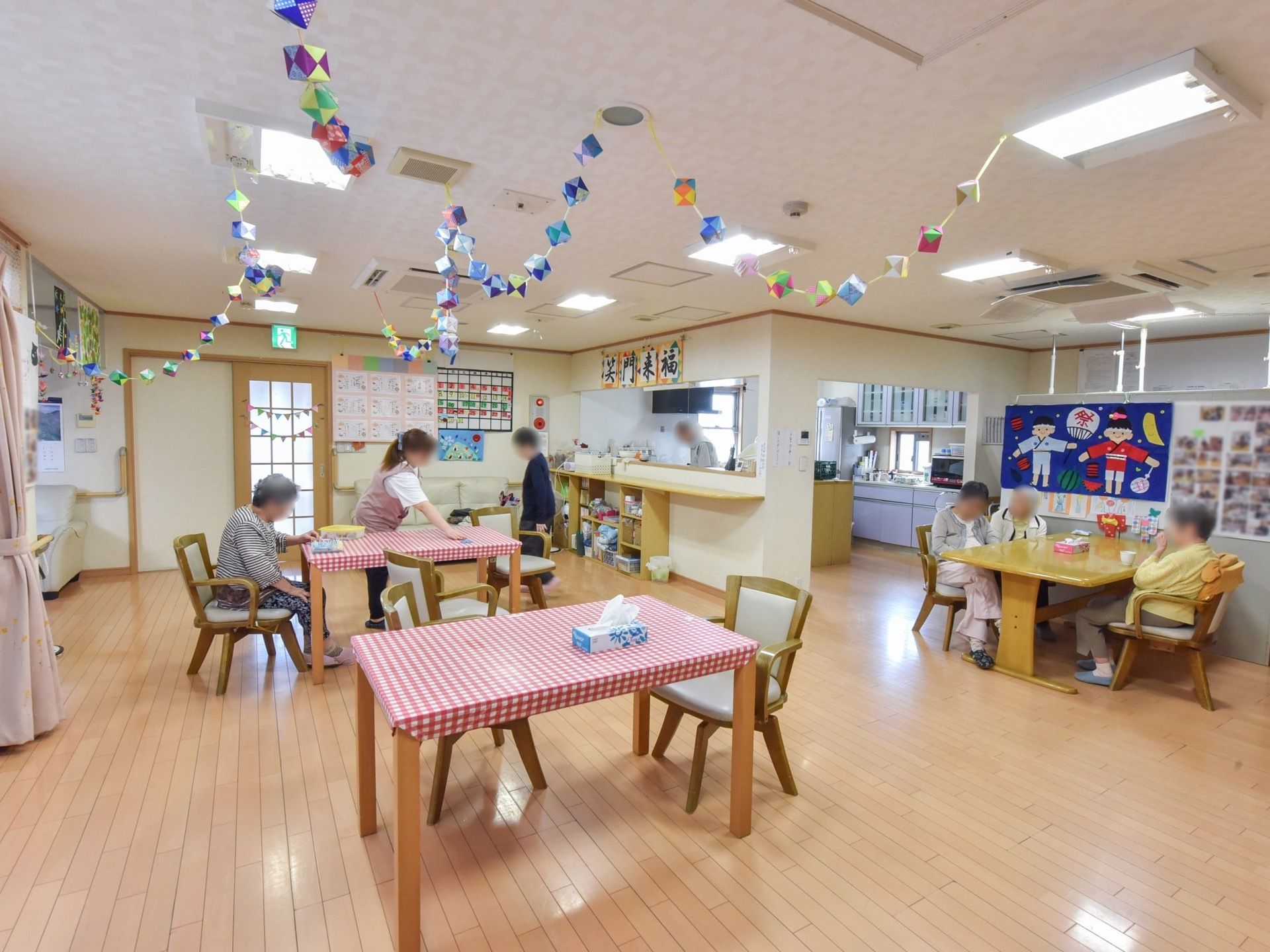 フローリング床の広い部屋に、テーブルと椅子が数組置かれている。天井には手作りの飾りが取りつけられている。