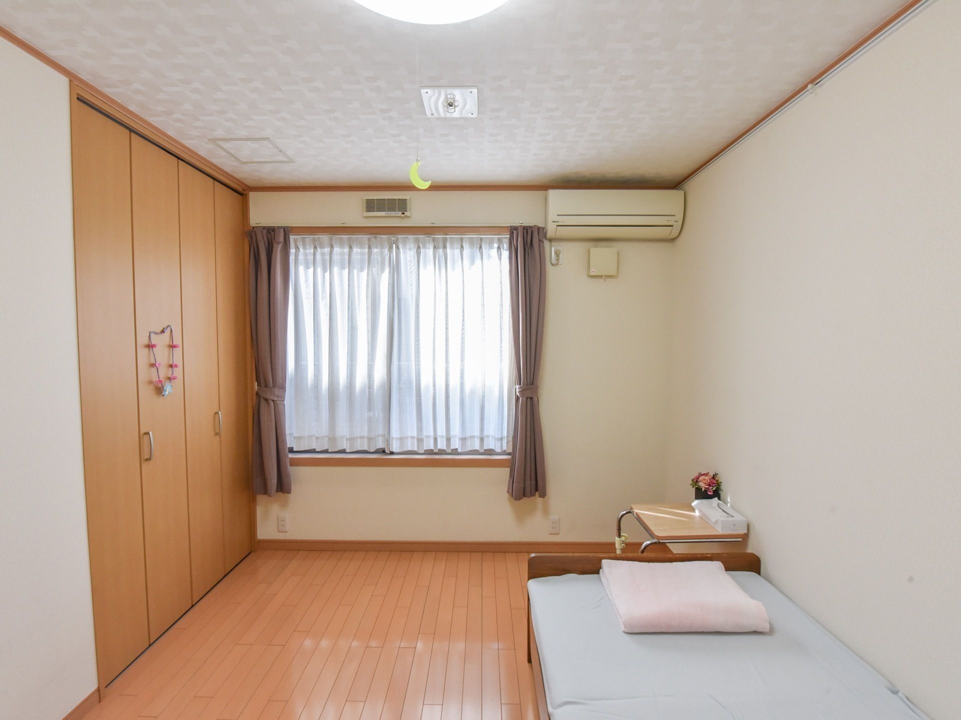フローリング床の部屋である。壁際にベッドが置かれ、通路が広くなっている。窓には赤紫とレースのカーテンが取りつけられている。