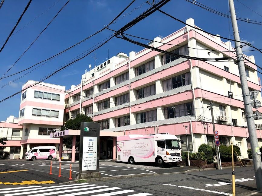 屋外で車いすに乗って散歩を楽しむ男性入居者とエプロン姿の女性スタッフ。二人とも笑顔。