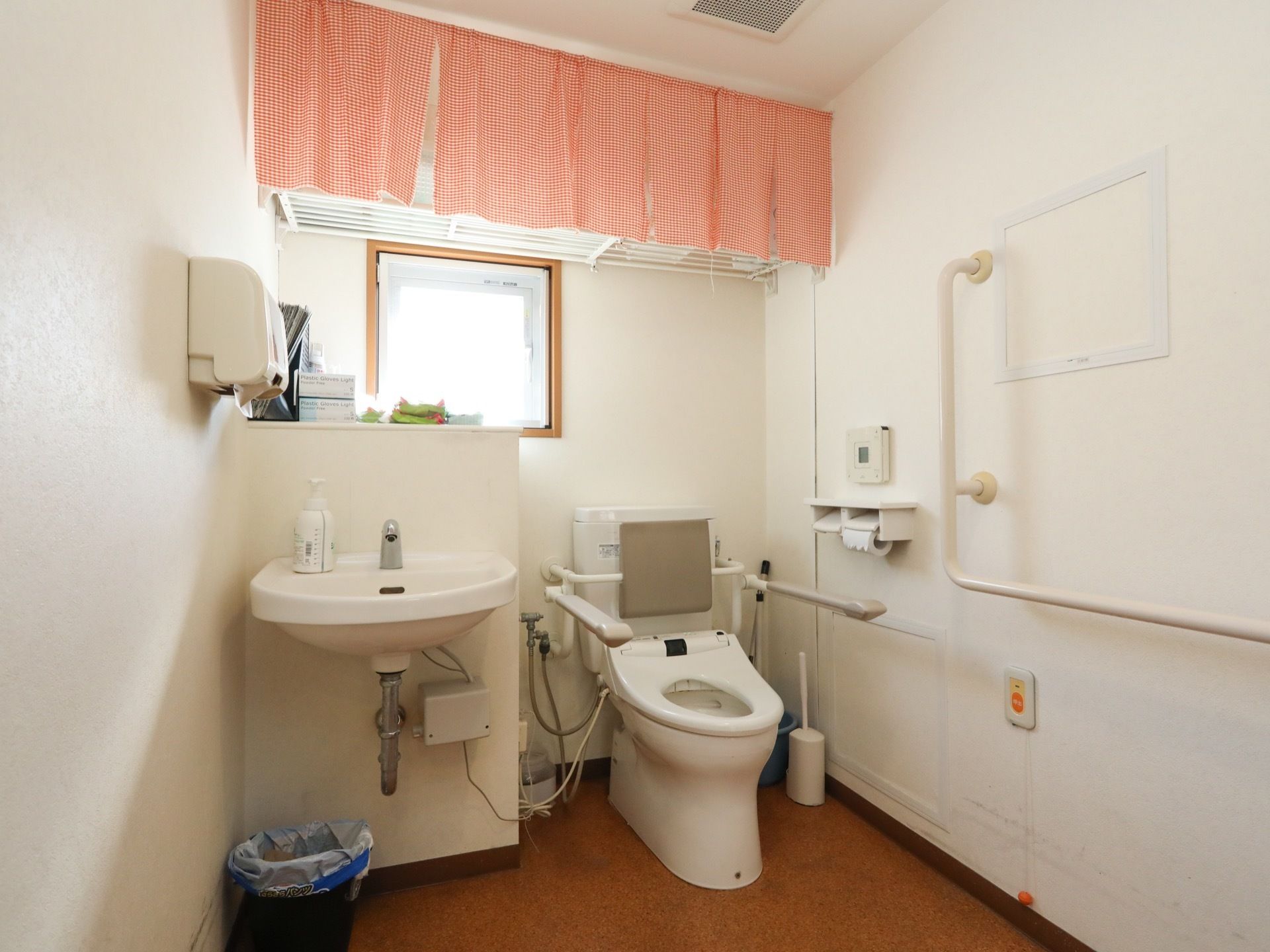 手洗い場付きの洋式トイレである。上部に収納スペースを確保。ピンク色の目隠しカーテンが備え付けられている。