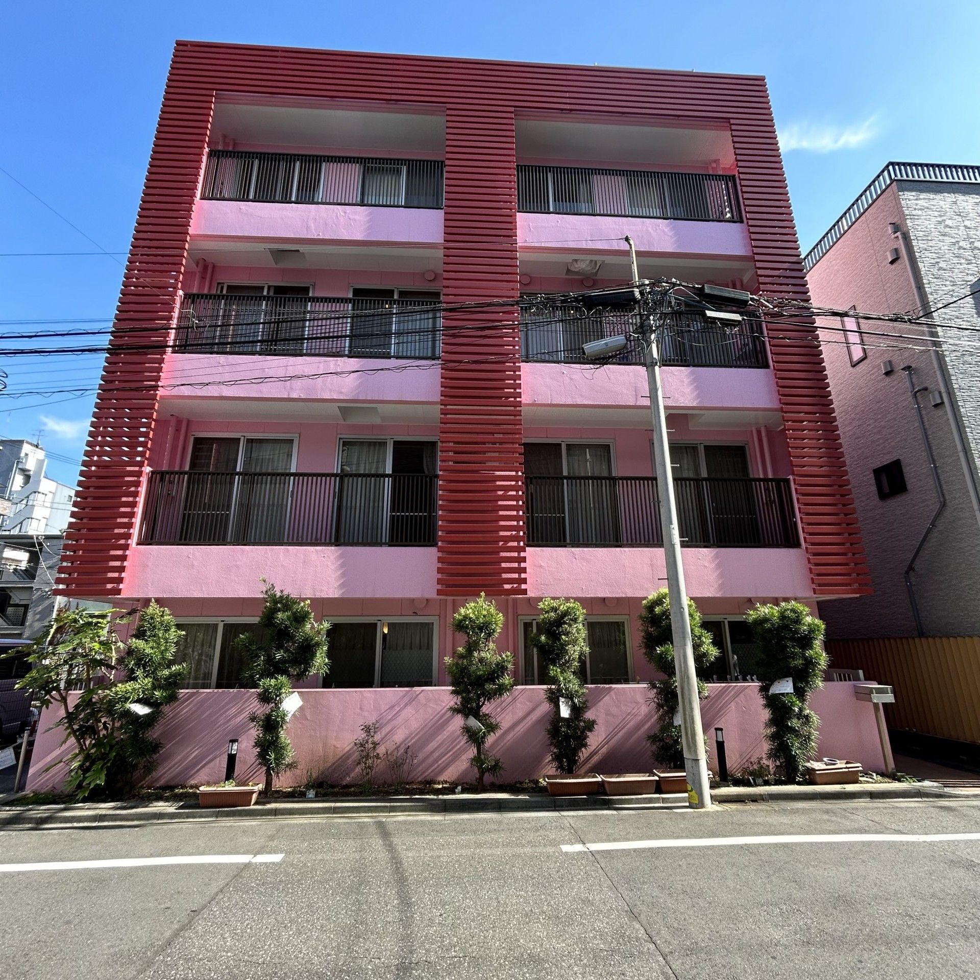 道路に面した場所に立地する、４階建ての施設である。庭木が随所に植えられている。となりには、コインパーキングがある。