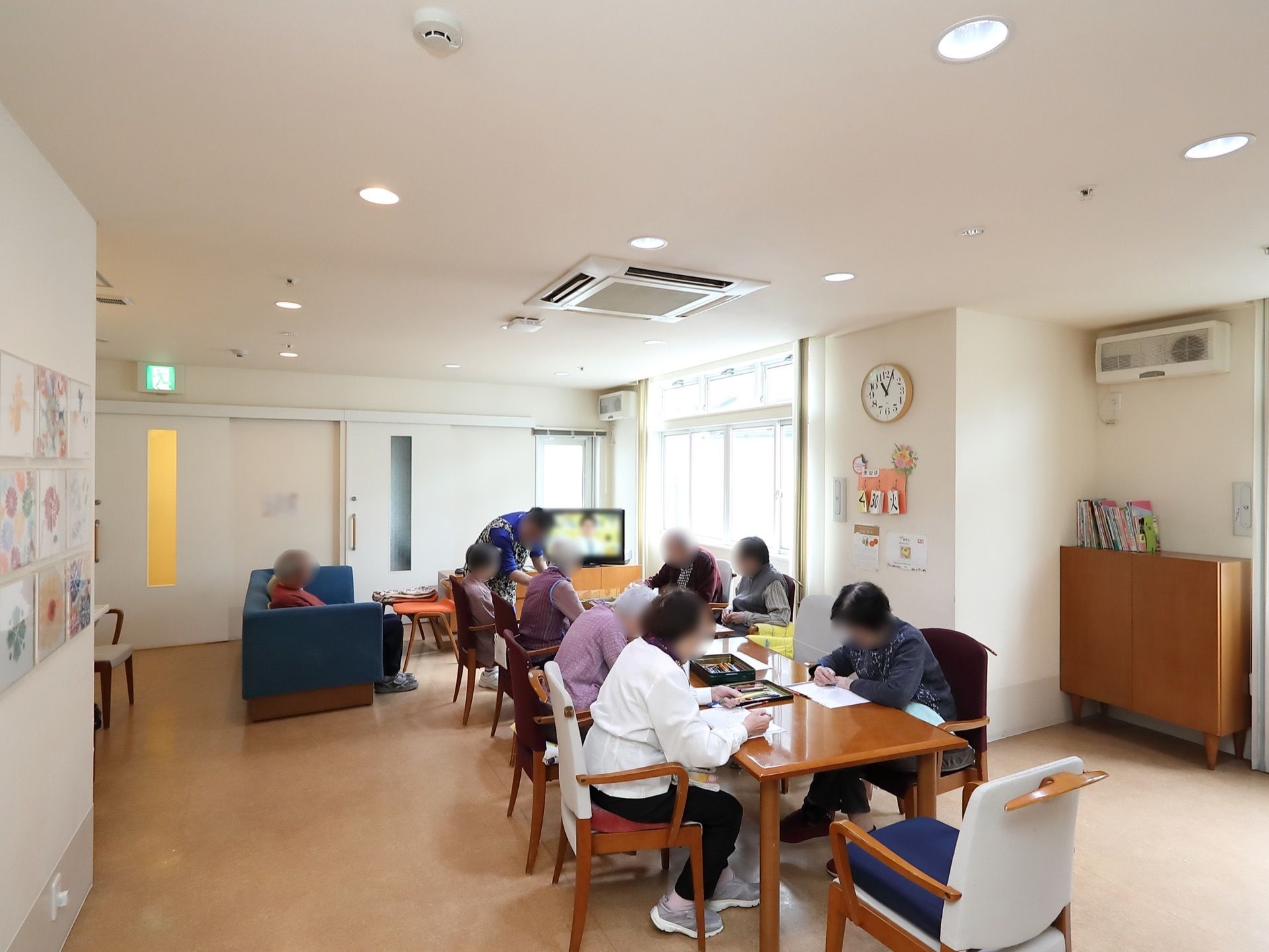 広々とした部屋の中央にテーブルを1列に並べ、入居者様が集まりレクリエーションに参加している。明るく開放的な空間でのんびり過ごせる。