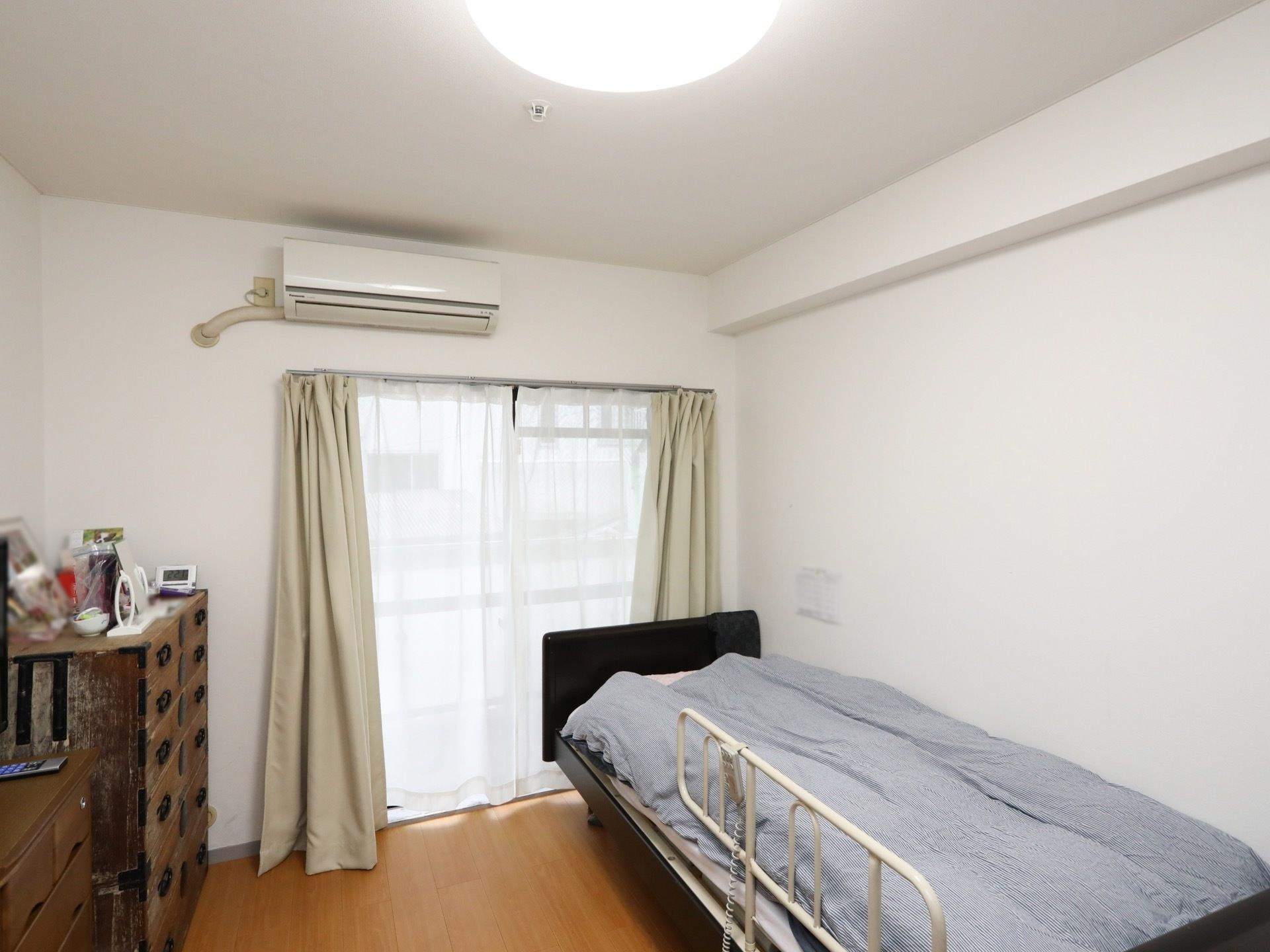 居室の左側には家具が配置され、反対側にはベッドが置かれている。カーテン越しに窓からは暖かい日の光が差し込む。
