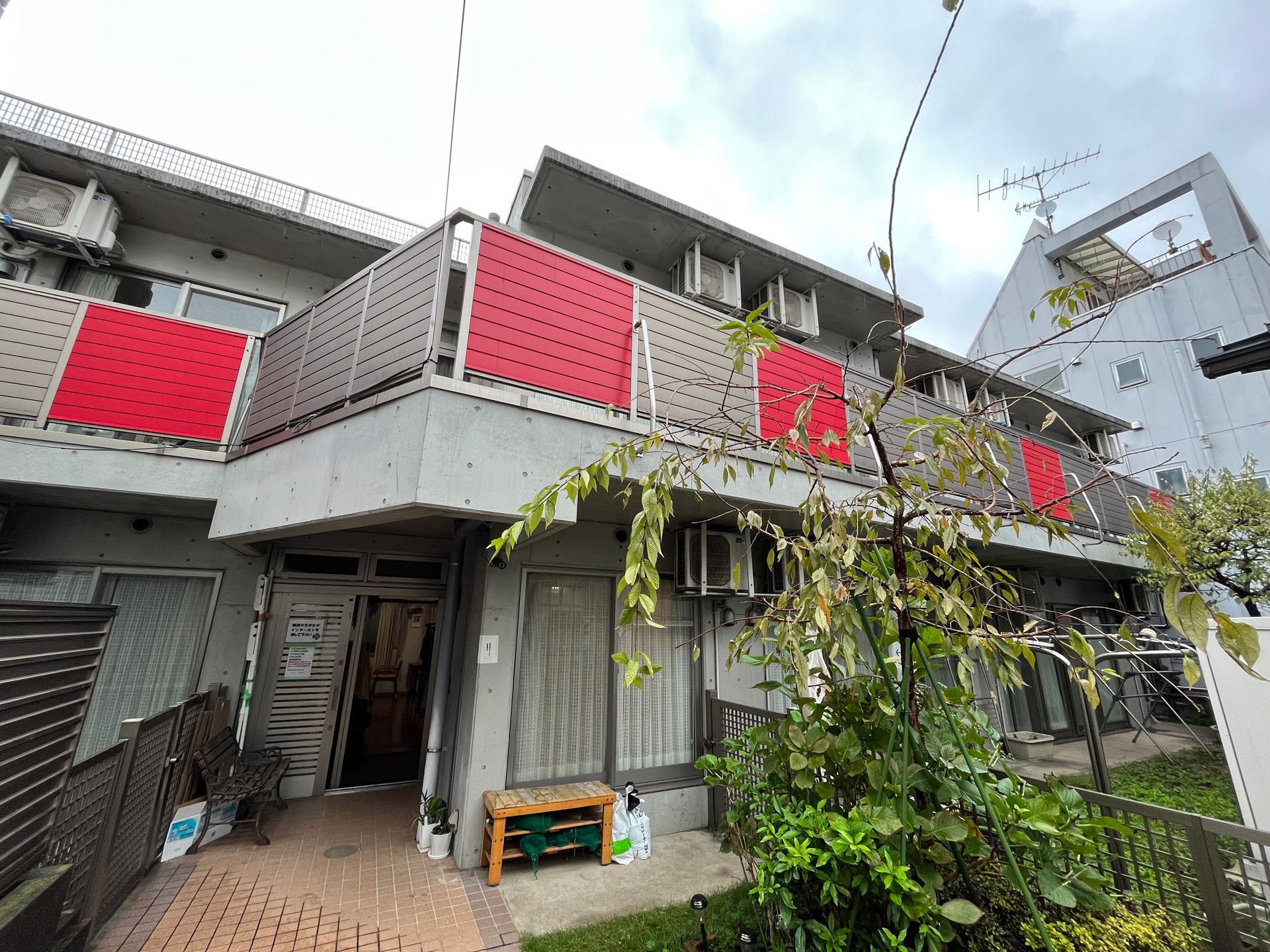 ベランダが付いた2階建ての建物の建っている敷地内には緑が植えられた庭もあり、明るい雰囲気。