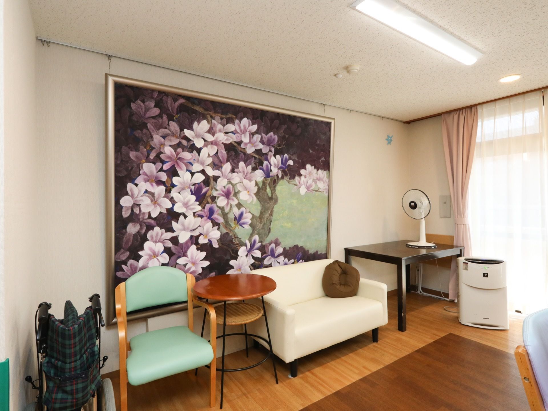 共有スペースの一角の壁面には、大きな花の絵が飾られている。その前にはソファやテーブルが並べられ、扇風機や空気清浄機も置かれている。