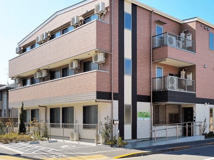 レンガ調のブラウンの外壁。3階建てで玄関先には手すり付きのスロープが設置されている。