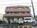 施設の建物側面の様子である。建物脇に駐車スペースが設けられている。車やバイク、自転車が停めてある。公道との間には、歩道が設けられている。