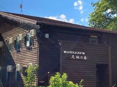 木材をふんだんに使用したログハウス調の2階建ての建物。上空には青空が広がり、緑に囲まれている。