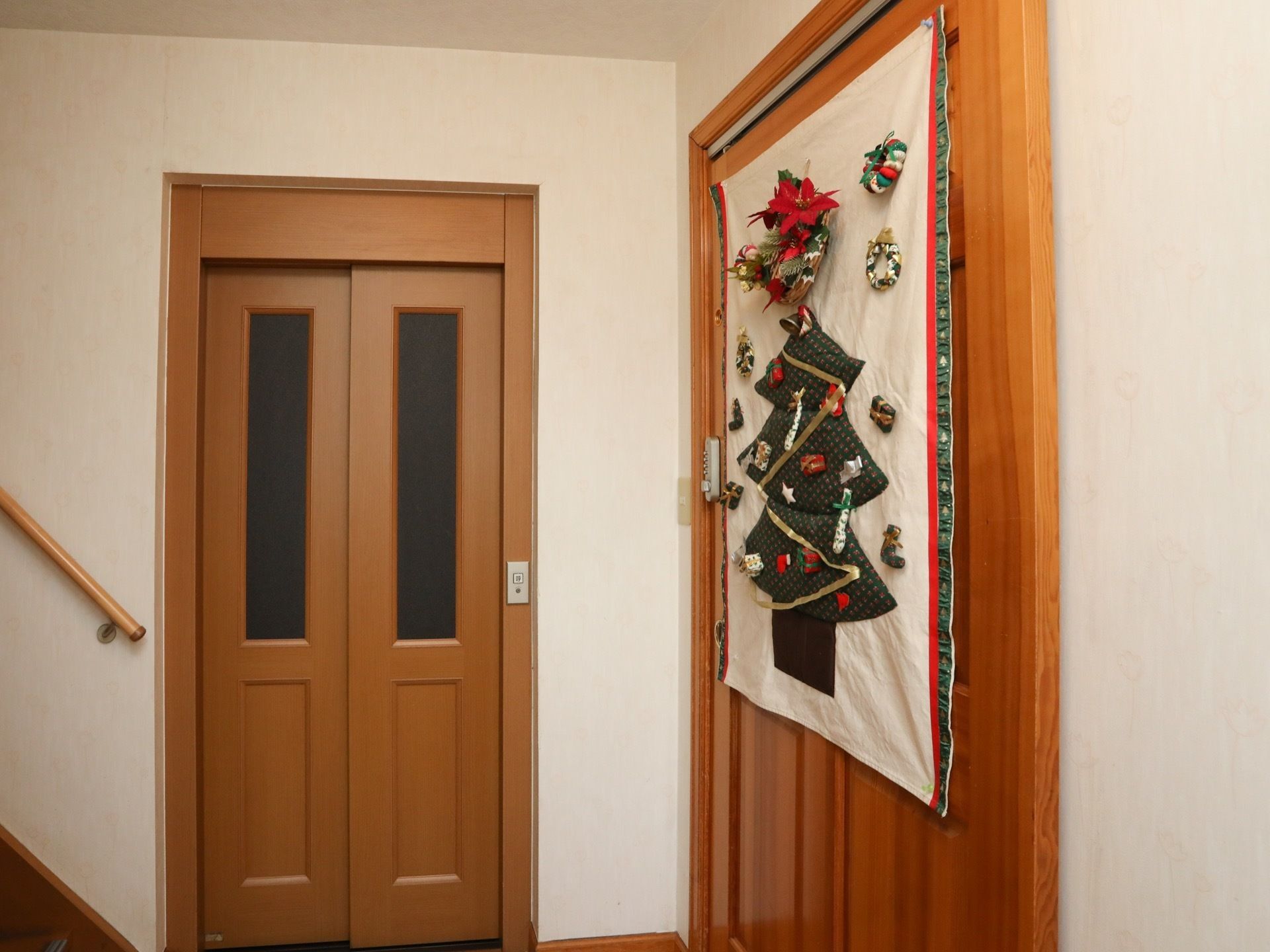 階段の横にエレベーターが設置されている。ドアは木目調で、エレベーターの横にはクリスマスのタペストリーが飾られている。