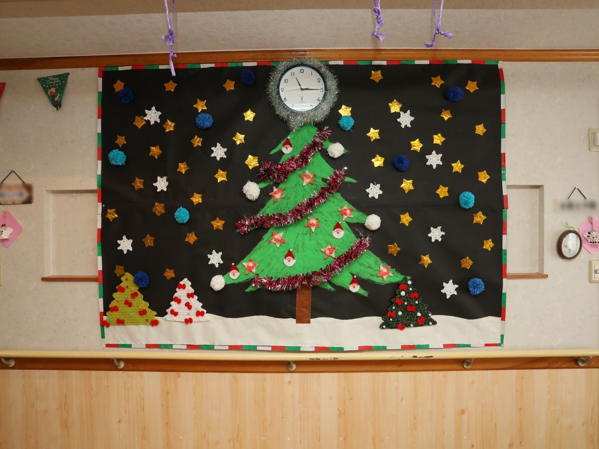 白い壁に時計がかけられており、時計を生かしたクリスマスをモチーフにした作品が飾られている。周囲にもクリスマスの飾り付けがされている。