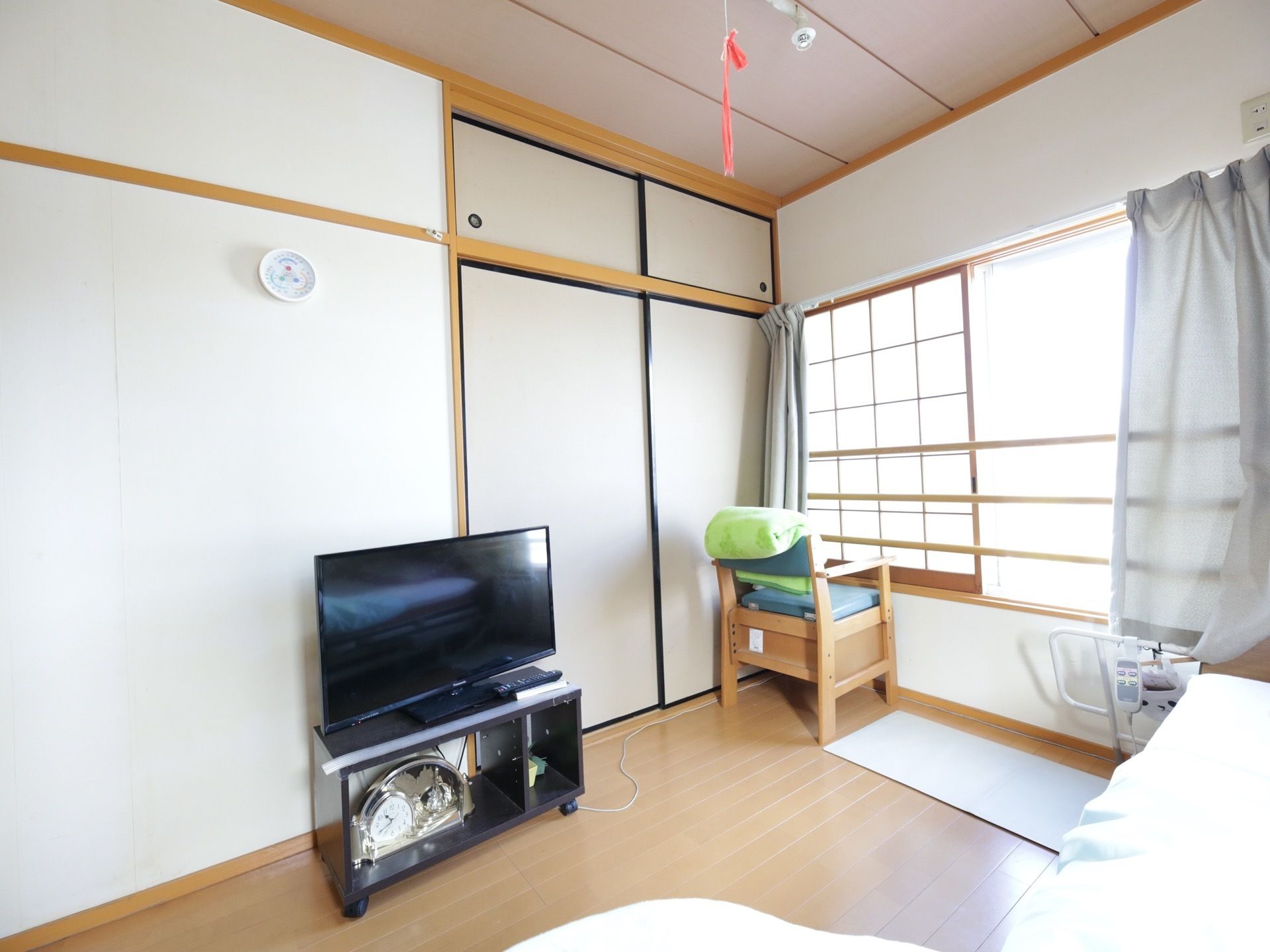 フローリングの居室に、ベッドとテレビが置かれている。ふすまや障子が設置されており、和と洋が混ざった部屋の造りになっている。